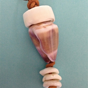 Puede incluir: Un llavero de cuero marrón con una cuenta de cerámica blanca, una concha y tres cuentas de cerámica blanca más.