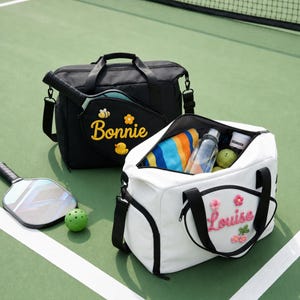 May include: A black holdall with the name Bonnie and embroidered bee, flower, and duck patches, and a white holdall with the name Louise and flower patches. Both bags feature black handles, zips, and side pockets for pickleball paddles.