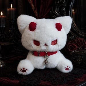 May include: A plush white cat toy with soft fur, featuring red embroidered eyes, red ear tips, and red paw pads. The cat wears a red collar with a silver-toned metal buckle and a small, round silver bell hanging from a metal ring at the centre.
