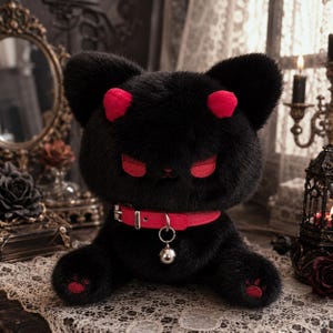 May include: A plush black cat toy with soft fur, featuring bright red accents on the ears, eyes, and paw pads. The cat wears a vibrant red collar with a silver-toned metal buckle and a small, round silver bell hanging from a central ring.