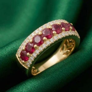 Puede incluir: Un anillo de banda de oro con una fila central de cinco rubíes redondos de color rojo intenso. Los rubíes están flanqueados por dos filas de pequeños diamantes blancos redondos y transparentes engastados en el metal dorado con acabado pulido.
