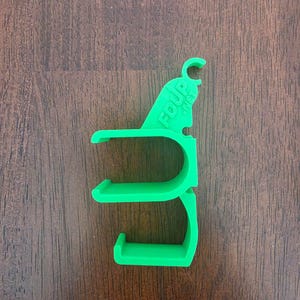 May include: A bright green plastic holder featuring two circular clips and a top hook, with the text FDUP.NET embossed on the upper section. The object has a rigid structure with an open design, intended for mounting or organizing items securely.