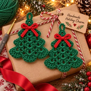May include: Two dark green crocheted Christmas tree ornaments with red yarn bows at the top. Each tree has a small loop for hanging. A brown paper gift tag is attached with the text Handmade Holiday Charm and a small red heart illustration.