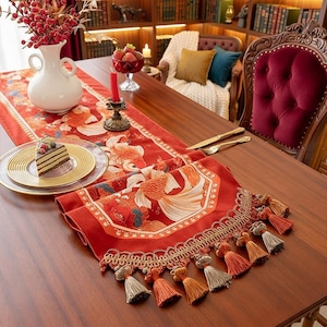 May include: Red table runner with a gold fish pattern and decorative tassels. The runner is on a wooden table, with a white vase, a plate with cake, and a red candle holder. The background includes a bookshelf and a red velvet chair.