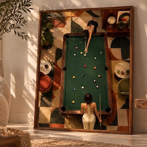 May include: A framed wall art print featuring an overhead view of a green pool table with scattered billiard balls. Two individuals are positioned at opposite ends of the table, one in a black top and one in a beige halter top, holding cues.