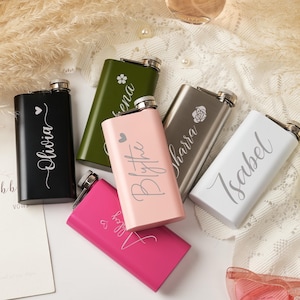 May include: A collection of six rectangular metal flasks in black, olive green, pink, metallic grey, and white. Each flask features a silver screw-top lid and is personalised with a unique name in white script, accompanied by small heart or floral icons.