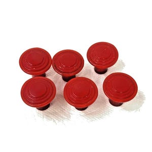 May include: Six red cabinet knobs with a circular, tiered design. The knobs are made of a solid material and have a glossy finish. These decorative knobs are suitable for furniture restoration or adding a pop of color to any room.