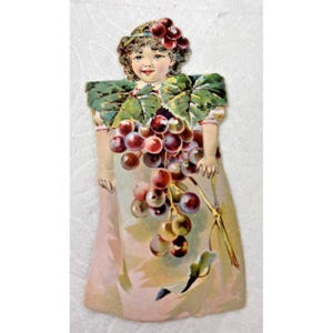 May include: Vintage die-cut illustration of a smiling girl adorned with grapes and grape leaves. The girl wears a headband of grapes and holds a large bunch of grapes. Her dress is a soft pink color.