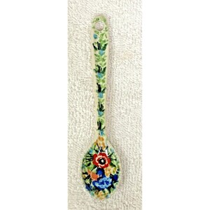 May include: A ceramic spoon featuring a hand-painted floral pattern with a cream-colored base. The handle is decorated with green leaves and blue accents, while the bowl displays a vibrant cluster of red, blue, and orange flowers and foliage.