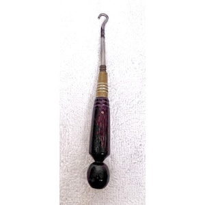 May include: A button hook tool featuring a slender metal shaft with a curved hook at the top. The handle is constructed from a dark, polished wood with a tapered, faceted design and a rounded base, accented by a metallic ferrule near the shaft.