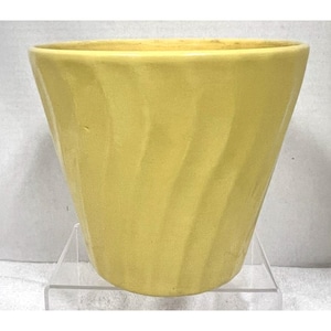 May include: A pale yellow ceramic planter with a slightly textured, swirled design. The planter has a wide opening and tapers down to a smaller base. The overall shape is a truncated cone.