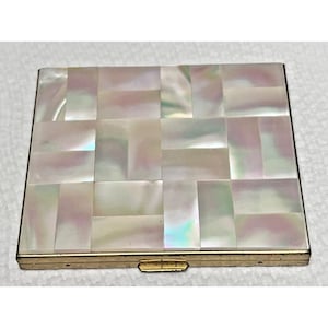 May include: A rectangular compact with a mosaic design. The surface is made of iridescent, rectangular mother-of-pearl tiles. The compact has a gold-colored metal frame and clasp. The tiles reflect a range of colors, including white, pink, and green.