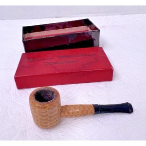 Könnte beinhalten: Eine Maiskolbenpfeife mit hellbraunem Kopf und dunkelblauem Mundstück, präsentiert mit einer roten Schachtel. Auf der Schachtel steht "Missouri Meerschaum Miniature". Die Pfeife hat ein klassisches Design.
