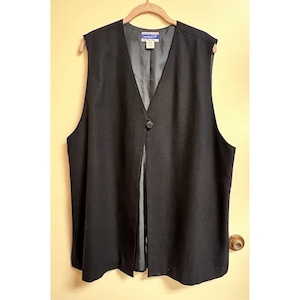 May include: A black sleeveless vest with a single button closure. The vest is made of a soft, textured fabric and has a long, flowing style.