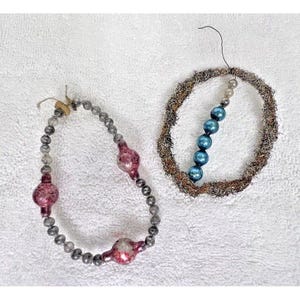 May include: Two vintage Christmas ornaments. One is a strand of gray beads with three red and white bulb ornaments. The other is a wreath made of brown twigs with a strand of blue beads.