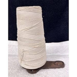 May include: A vintage white thread spool with a metal base. The spool is made of a woven material and is attached to a metal base with a screw.