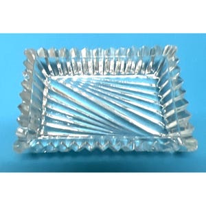 May include: A clear, rectangular glass dish with a textured, ridged design. The dish has a scalloped edge and a diagonal pattern on the interior. The background is a solid blue.