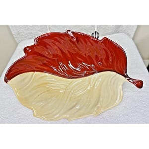 May include: A ceramic leaf-shaped serving dish with a red and cream glaze. The dish is designed to look like a leaf with a raised vein pattern.