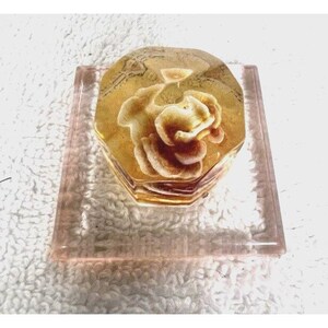 May include: A clear glass box with a rose-shaped design inside. The box is on a clear glass base with a pink tint.