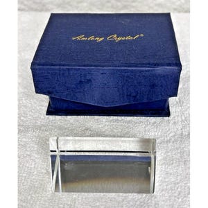 May include: A clear glass paperweight with beveled edges in a blue velvet box with the text "Amory Crystal" in gold lettering.