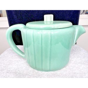 May include: A light green ceramic teapot with a lid and a ribbed design. The teapot has a handle and a spout.