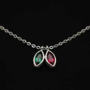 May include: A silver chain necklace featuring two marquise-cut gemstones suspended from the center. One gemstone is a deep emerald green, and the other is a vibrant ruby red. Both stones are set in polished silver bezels on a delicate link chain.