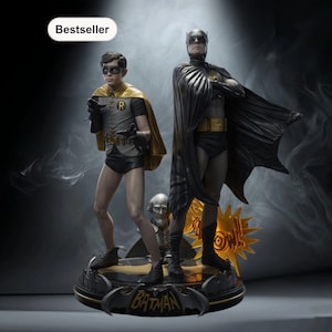 Puede incluir: Una estatua de Batman y Robin sobre una base negra y dorada. La figura de Batman lleva una capa y una capucha negras. Robin lleva una capa amarilla y un atuendo gris y negro. La base tiene la palabra "Batman".