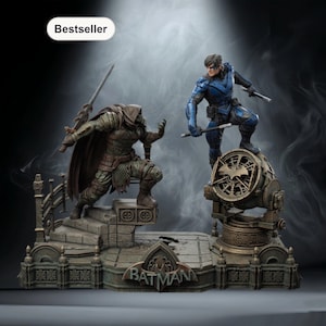 Op de afbeelding: Een gedetailleerd beeld met een gevechtsscène. Eén figuur draagt groene bepantsering, de andere blauwe. De basis is gegraveerd met "BATMAN". Het woord "Bestseller" staat linksboven.