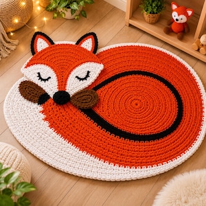 May include: A handmade, oval-shaped rug featuring a sleeping fox design. The rug is primarily orange, with white, black, and brown accents. The fox's head is at one end, with closed eyes and a black nose. The rug measures approximately 40 inches in length.
