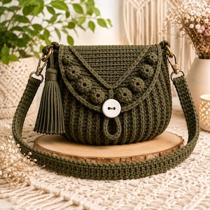 May include: An olive green crochet crossbody bag featuring a ribbed body, a flap adorned with a row of raised circular bobble stitches, a large white two-hole button closure, a matching side tassel, and a thick, sturdy crocheted shoulder strap.