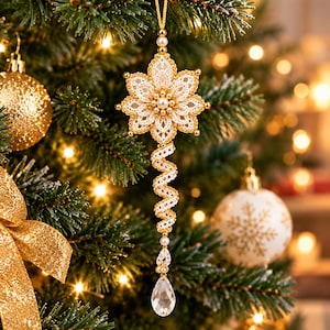 May include: A hanging Christmas tree ornament featuring a white lace flower with gold-toned edges and a central pearl cluster. A spiraling lace ribbon extends downward, ending in a clear, teardrop-shaped crystal bead with gold accents.