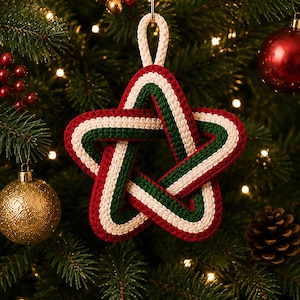 May include: A five-pointed star ornament crafted from braided cord in alternating stripes of red, white, and dark green. The star features a continuous, interwoven design with a matching braided loop at the top for hanging on a tree branch.