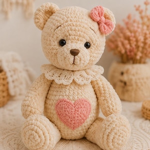 May include: A cream-coloured crocheted teddy bear featuring a soft texture, a pink heart patch on its chest, a pink bow on its left ear, and a white lace collar around its neck. The bear has dark brown plastic eyes and a brown stitched nose.