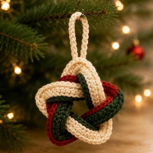 May include: A star-shaped hanging ornament crafted from crocheted yarn in cream, dark green, and deep red colours. The design features an intricate, interwoven knot pattern with a matching cream-coloured braided loop at the top for hanging.