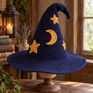 Peut inclure: Un chapeau pointu en crochet bleu foncé orné d'appliqués en forme d'étoiles et de croissant de lune jaunes. Le chapeau présente un large bord et une couronne haute légèrement courbée, réalisée avec un point de tricot texturé visible.
