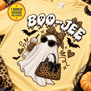 May include: A pale yellow t-shirt featuring a graphic of a ghost wearing leopard print sunglasses and a matching bow, holding a leopard print coffee cup and handbag. The text reads BOO-JEE, surrounded by bats, hearts, and a 1 BONUS DESIGN INCLUDED badge.