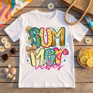 Peut inclure: Un t-shirt blanc à manches courtes avec le texte SUMMER VIBES en grandes lettres à motifs variés. Le design inclut des motifs dorés, à damier, tropicaux et tie-dye, agrémenté de petites marguerites, d'un nœud beige et d'un soleil.