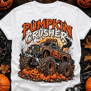 May include: A white t-shirt featuring a graphic of a black monster truck with orange flame accents and a pumpkin design on the side. The text PUMPKIN CRUSHER appears above the truck, which is surrounded by pumpkins, bare trees, and smoke.