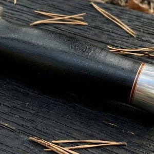 May include: A fixed-blade knife handle featuring a smooth black grip, polished silver-toned metal bolsters at both ends, and thin copper-colored accent rings separating the handle sections from the metallic components.