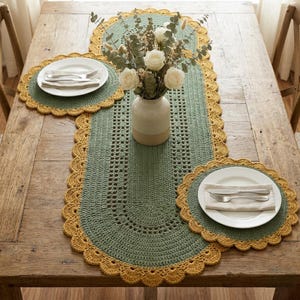 May include: A handmade crochet table runner and placemats set in sage green with a mustard yellow scalloped edge. The table is set with white plates, silverware, and a vase of white roses.