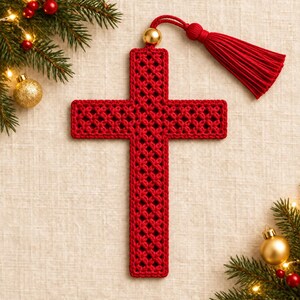 May include: A red crocheted cross ornament featuring an intricate openwork lattice pattern. The cross is topped with a gold-toned bead and a long, matching red fabric tassel. The design is uniform in color and texture throughout the piece.