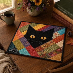 May include: A quilted placemat featuring a black cat face with yellow eyes. The cat is set against a patchwork background of various fabric patterns and colors, including orange, red, and blue. The placemat has a black border.