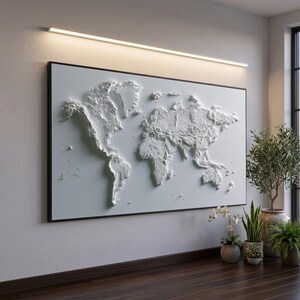 Peut inclure: Une grande œuvre d'art murale rectangulaire présentant une carte du monde en relief blanc en trois dimensions. Les continents sont en relief sur le fond blanc plat, créant des ombres et de la profondeur. L'œuvre est encadrée d'un fin bord noir.