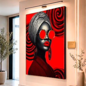 Pode incluir: Um retrato marcante sobre um fundo vermelho apresenta uma mulher com um turbante prateado, óculos de sol vermelhos e batom vermelho. A obra de arte inclui desenhos em espiral pretos e vermelhos e é emoldurada em preto.