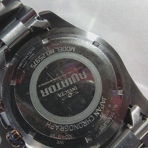 May include: Close-up of the back of a stainless steel Invicta Aviator chronograph watch. The watch features the text "AVIATOR" and "JAPAN CHRONOGRAPH". The watch is water resistant to 100 meters.