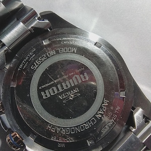 May include: Close-up of the back of a stainless steel Invicta Aviator chronograph watch. The watch features the text "AVIATOR", "JAPAN CHRONOGRAPH", and "MODEL NO.25975". The watch has a silver band and a black face.