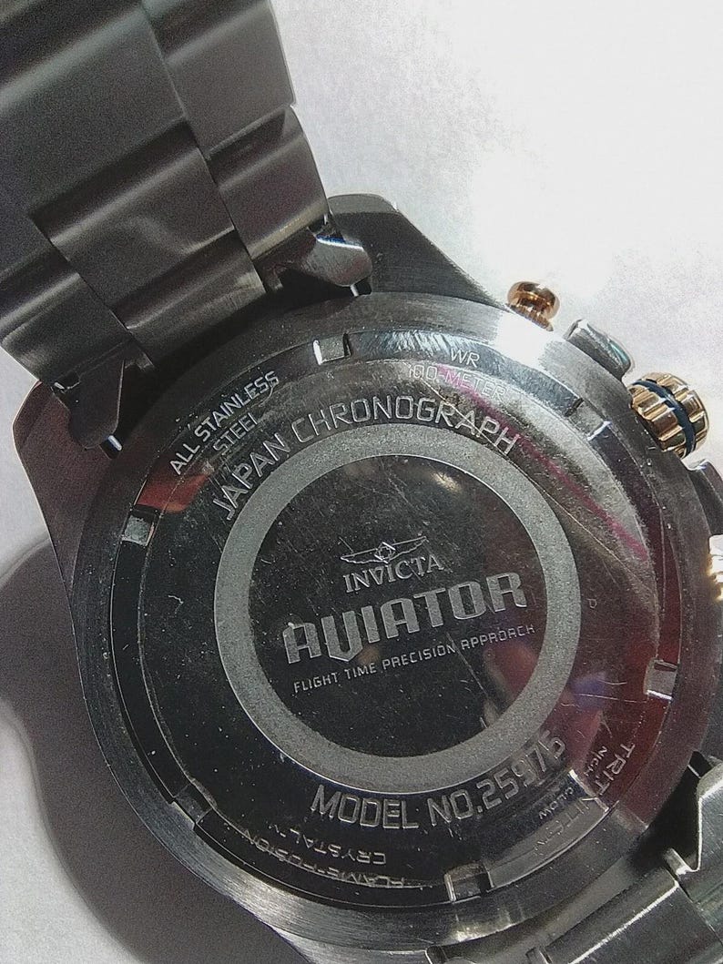 May include: Close-up of the back of a stainless steel Invicta Aviator chronograph watch. The watch features the text "All Stainless Steel", "Japan Chronograph", and "Aviator". The model number is 25975.