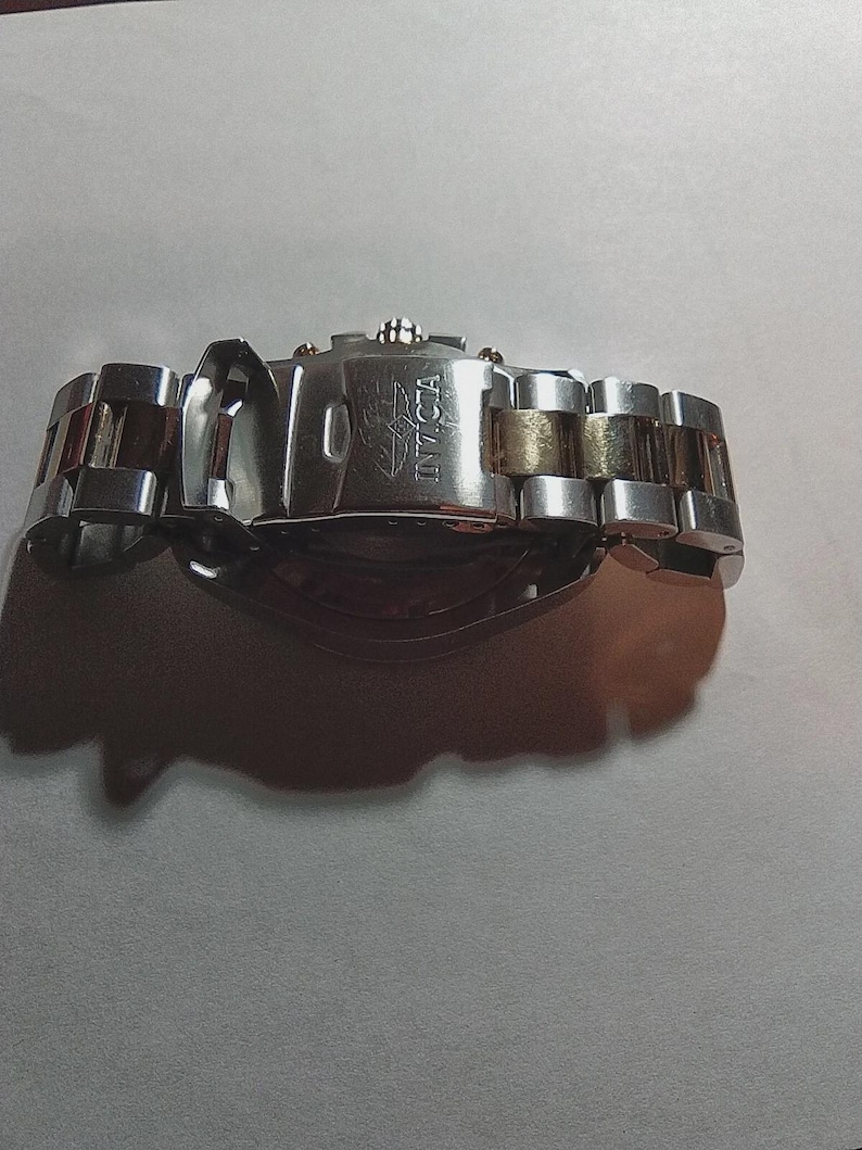 May include: A silver and gold Invicta watch with a stainless steel band. The watch clasp is open, revealing the Invicta logo. The watch band has silver and gold links.