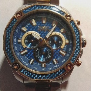 May include: A stainless steel Invicta watch with a blue and gold face. The watch features a blue carbon fiber bezel and three sub-dials. The watch has gold accents and a stainless steel band.