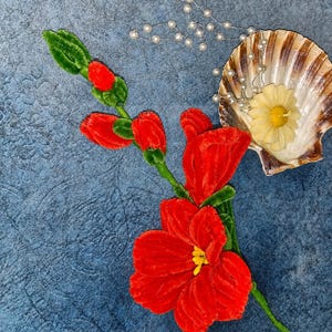May include: A vibrant red velvet flower stem with green leaves and buds, accompanied by a delicate silver-toned chain featuring small white faux pearls and a pale yellow flower-shaped candle resting inside a natural scalloped seashell.